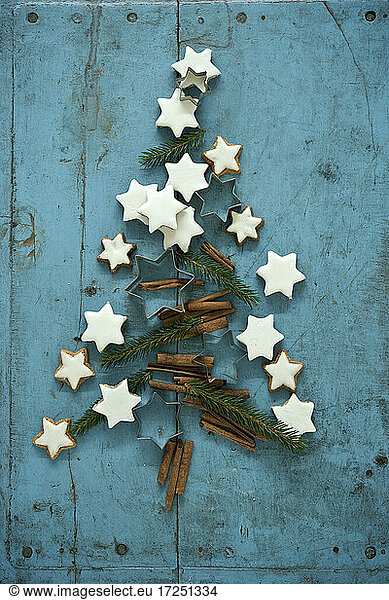 Christmas cinnamon star shaped cookies together with cinnamon and needle branches arranged in Christmas Tree on blue rustic wooden background