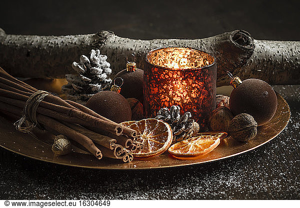 Christmas decoration with tea light candle  christmas tree balls  cinnamon sticks  slices of dried oranges and walnuts on plate  studio shot