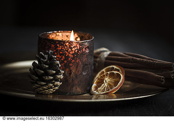 Christmas decoration with tea light candle  cinnamon sticks  slices of dried oranges and cone on plate  studio shot