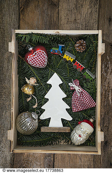 Christmas decorations lying inside crate filled with conifer twigs