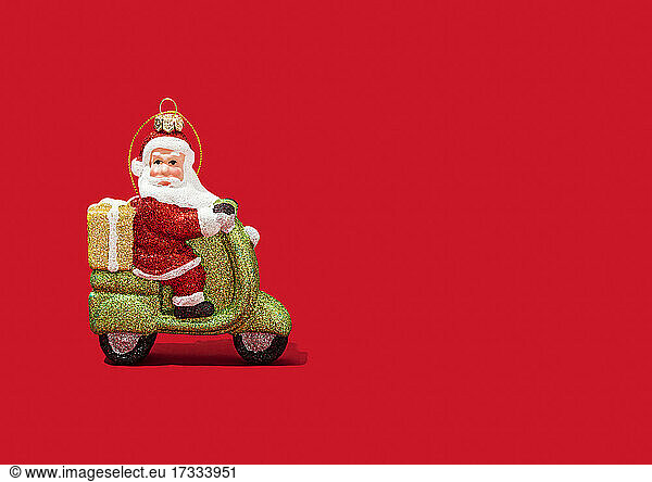 Christmas ornament of Santa Claus riding motor scooter against vibrant red background
