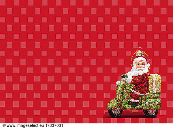 Christmas ornament of Santa Claus riding motor scooter against vibrant red checked background