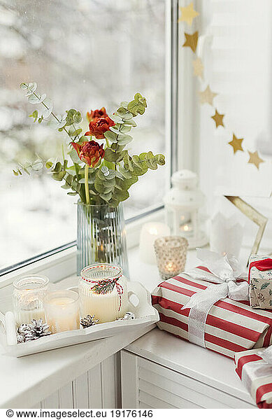 Christmas presents and candles with red tulips near window