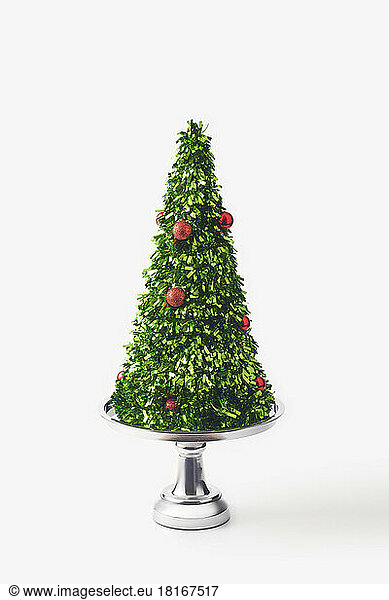 Christmas tree made of green confetti on silver cakestand against white background