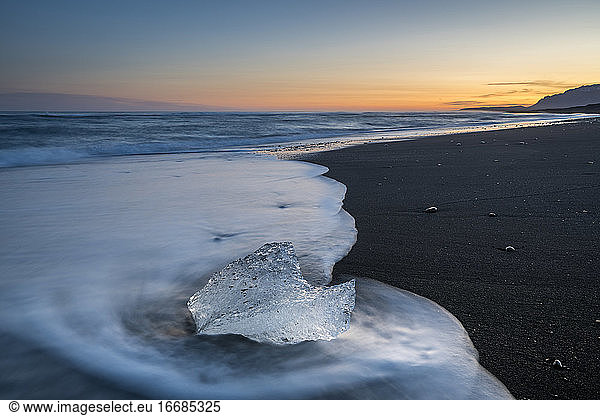 Chunk of ice on sea shore at Diamond beach near Jokulsarlon Glacier Lagoon at sunset  Iceland