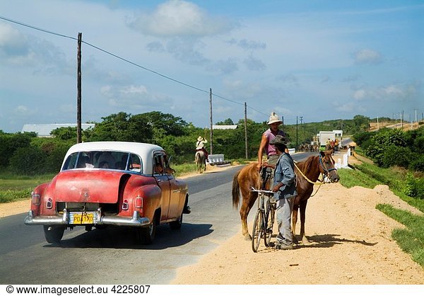 Classic American car passing by a cowboy and a biker talking on a countryside road  Cuba