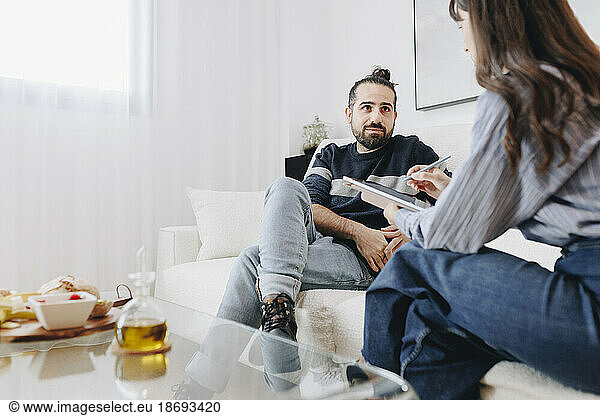 Client listening to nutritionist sitting on sofa at home