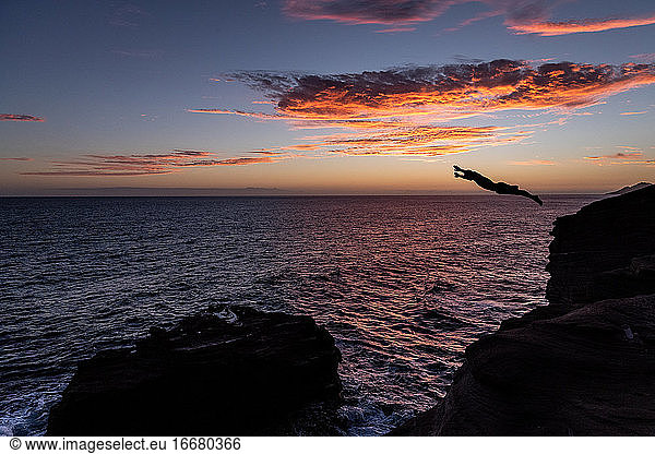 Cliff diver over the ocean at sunset in Hawaii