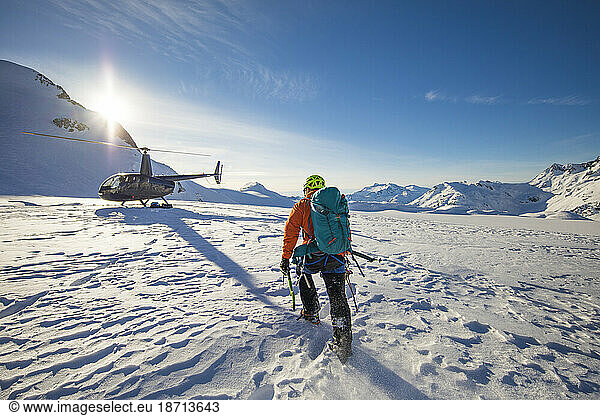 Climber approaches a helicopter  landed on a glacier for a luxury tour