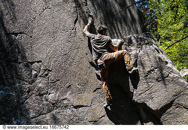 Climber is getting to the top of the granite boulder in Washington