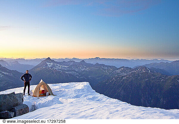 Climber standing next to tent on mountain summit Whistler Canada.