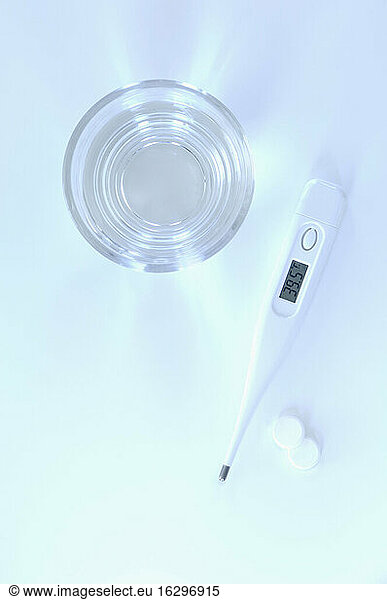 Clinical thermometre with glass of water and tablets  close up