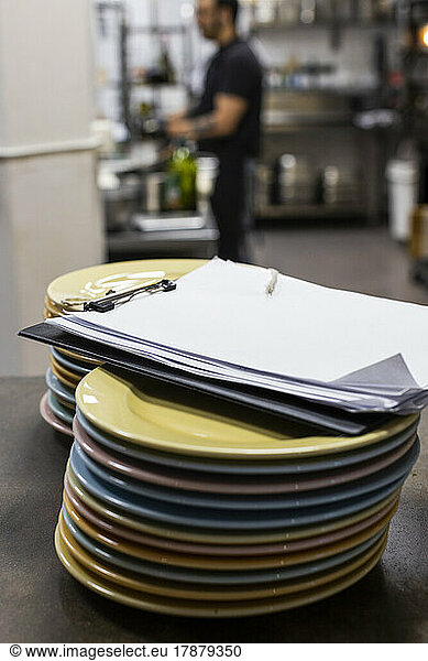 Clipboard on stack of plates on kitchen counter in restaurant
