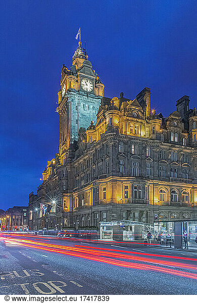 Clock tower of Balmoral Hotel lit up at night with traffic light blur below.