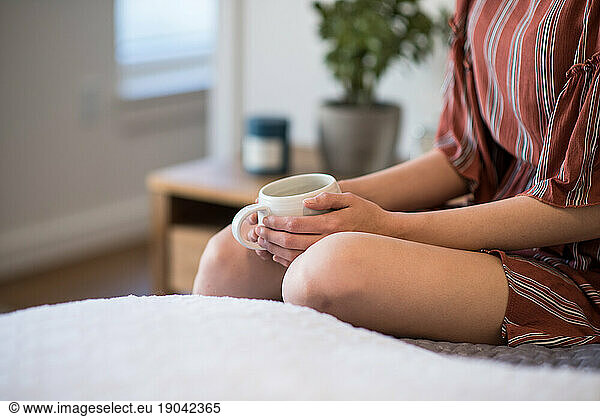 Close frame of woman sitting on bed holding coffee mug
