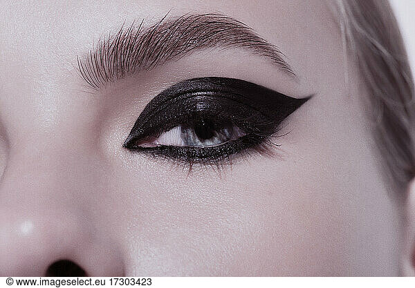 Close-up beauty shot of eye of a young pretty model with bright cat-eye make-up. Black Eyeliner. Pink lips. Gorgeous beauty portait