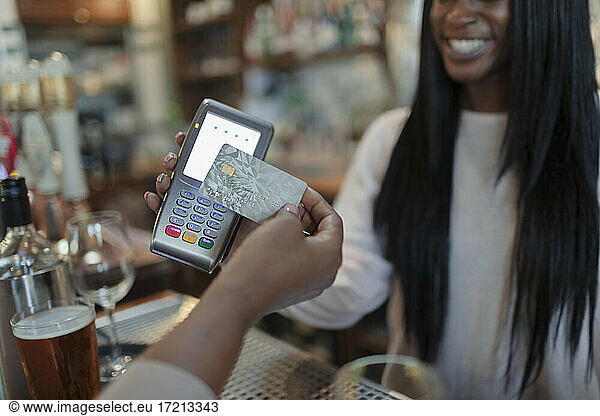 Close up customer paying female bartender with smart card in pub
