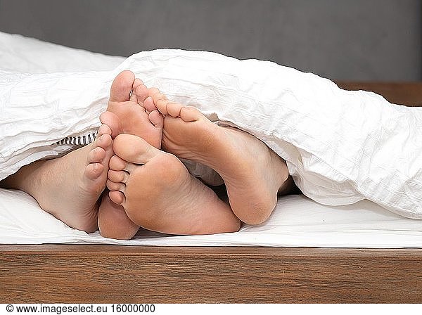 Close up feet of a couple under the white sheets blanket in bed  sex hugging and partner valentines concept sexy and romantic.