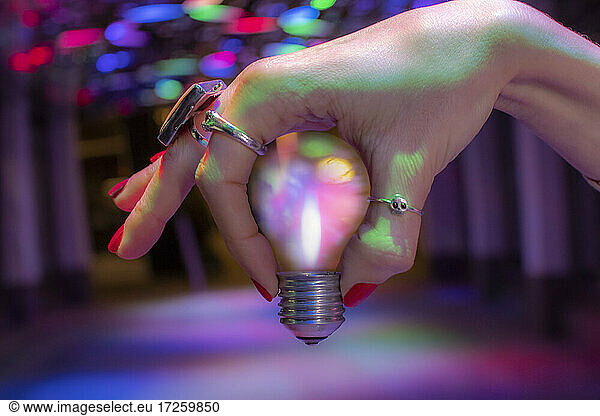 Close up hand holding light bulb under neon light