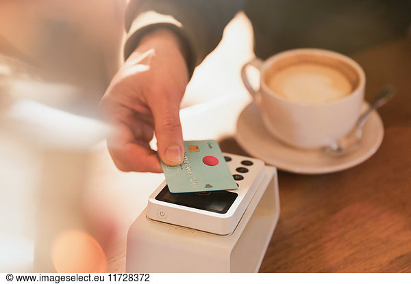 Close up man paying for cappuccino with credit card contactless payment in cafe