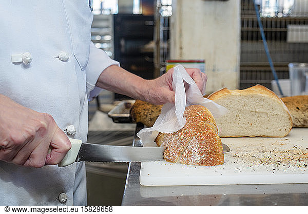 Close-up of a baker in a white chef's coat slicing fresh bread