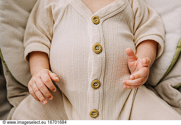 Close up of a big full baby belly in cream colored outfit with buttons