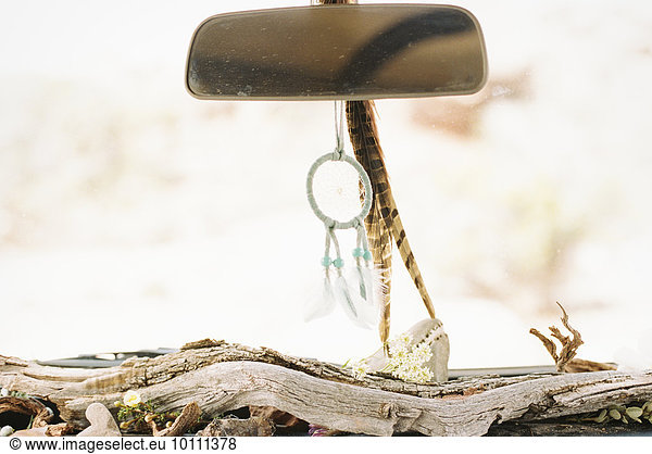 Close up of a car interior  driftwood on the dashboard  a dream catcher and feathers hanging from the rear view mirror.