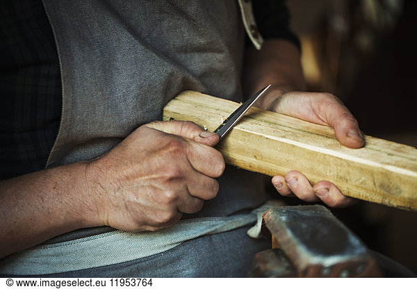 Close up of a craftsman cutting and paring the corners of a piece of wood with a sharp carving knife.