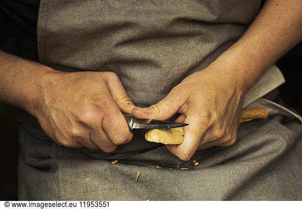 Close up of a craftsman's hands pressing and shaping a small piece of wood into a spoon with a sharp knife blade  shaping the bowl back.