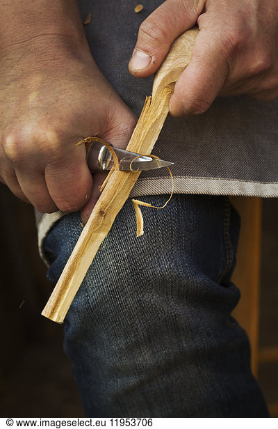 Close up of a craftsman shaping a small piece of wood with a sharp carving knife.