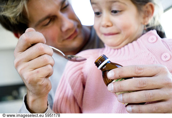Close-up of a father giving syrup in a spoon to her daughter. Close-up of a father giving syrup in a spoon to her daughter