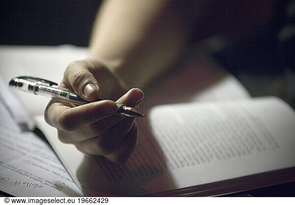 Close-up of a hand holding a pen  resting on a open book.