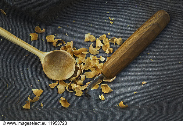 Close up of a handmade handcarved wooden spoon with round bowl end  a sharp carver's knife and wood shavings.