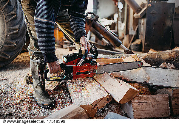 Close-up of a man cutting firewood with a chainsaw.