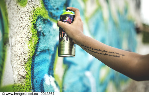 Close up of a person spray painting a graffiti tag onto a wall.