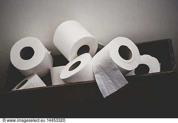 Close up of a pile of toilet paper rolls in a brown wooden crate.