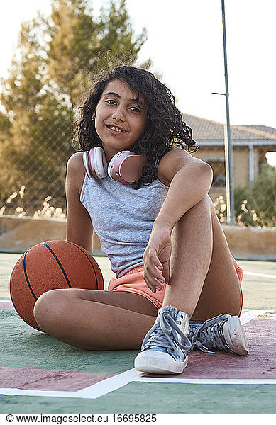 Close-up of a sitting girl with curly hair with a basketball and headphones