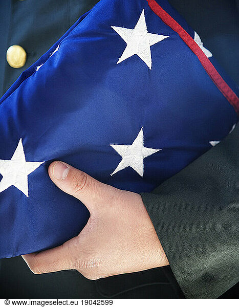 Close up of a soldier holding a folded American flag at his side.