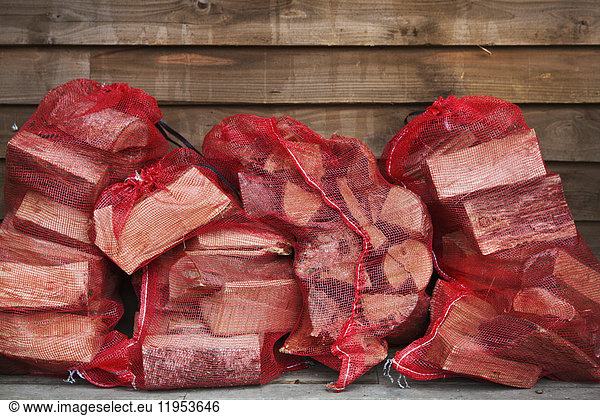 Close up of a stack of firewood in red net bags outside a farm shop.