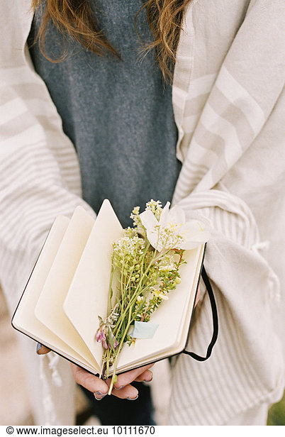 Close up of a woman holding a notebook with wild flowers lying between the pages.