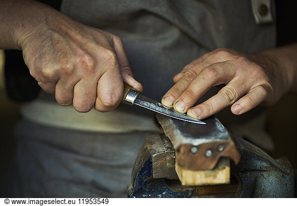 Close up of a wood carver honing the blade of a carver's knife on a leather strop  pressing the blade down  sharpening his tools.