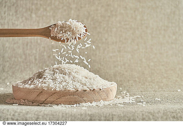 Close up of a wooden spoon pouring raw white rice on a wooden plate