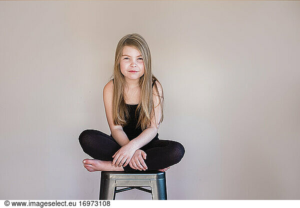Close up of a young girl sitting cross legged on a stool