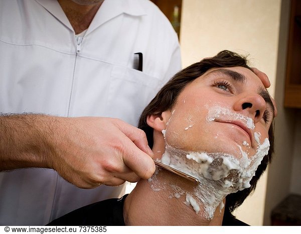 Close_up of a young man getting a shave at a barber
