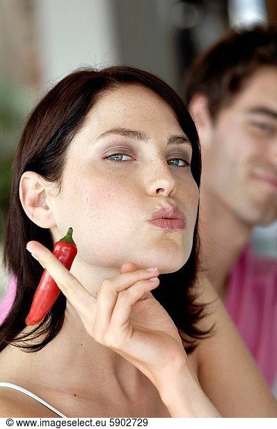 Close_up of a young woman pretending to smoke a cigarette with a young man in the background