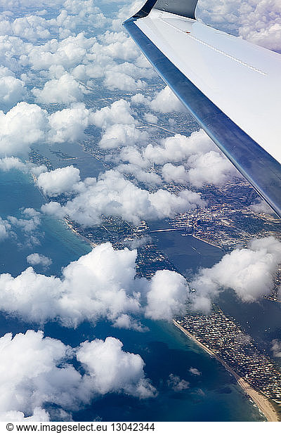 Close-up of aircraft wing flying in cloudy sky over cityscape and sea
