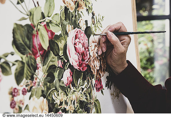 Close up of artist working on painting of pink tea roses  leaves  berries and other flowers.