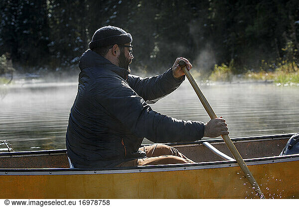 Close up of bearded man paddling canoe on a foggy lake in Canada