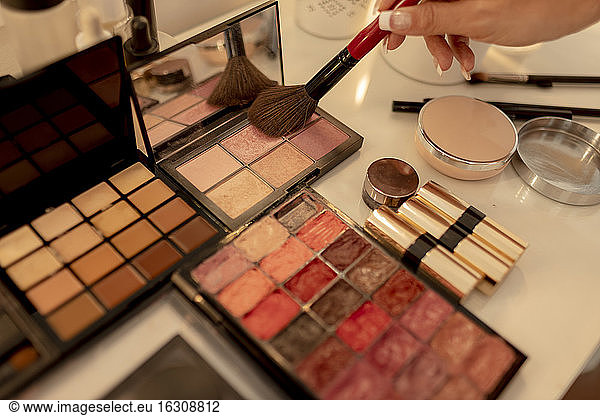 Close-up of beautician's hand with make-up brush and beauty products on dressing table