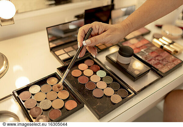 Close-up of beautician's hand with make-up brush and palettes on dressing table
